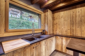 A kitchen with wooden cabinetry, a double sink, and a window overlooking a garden.