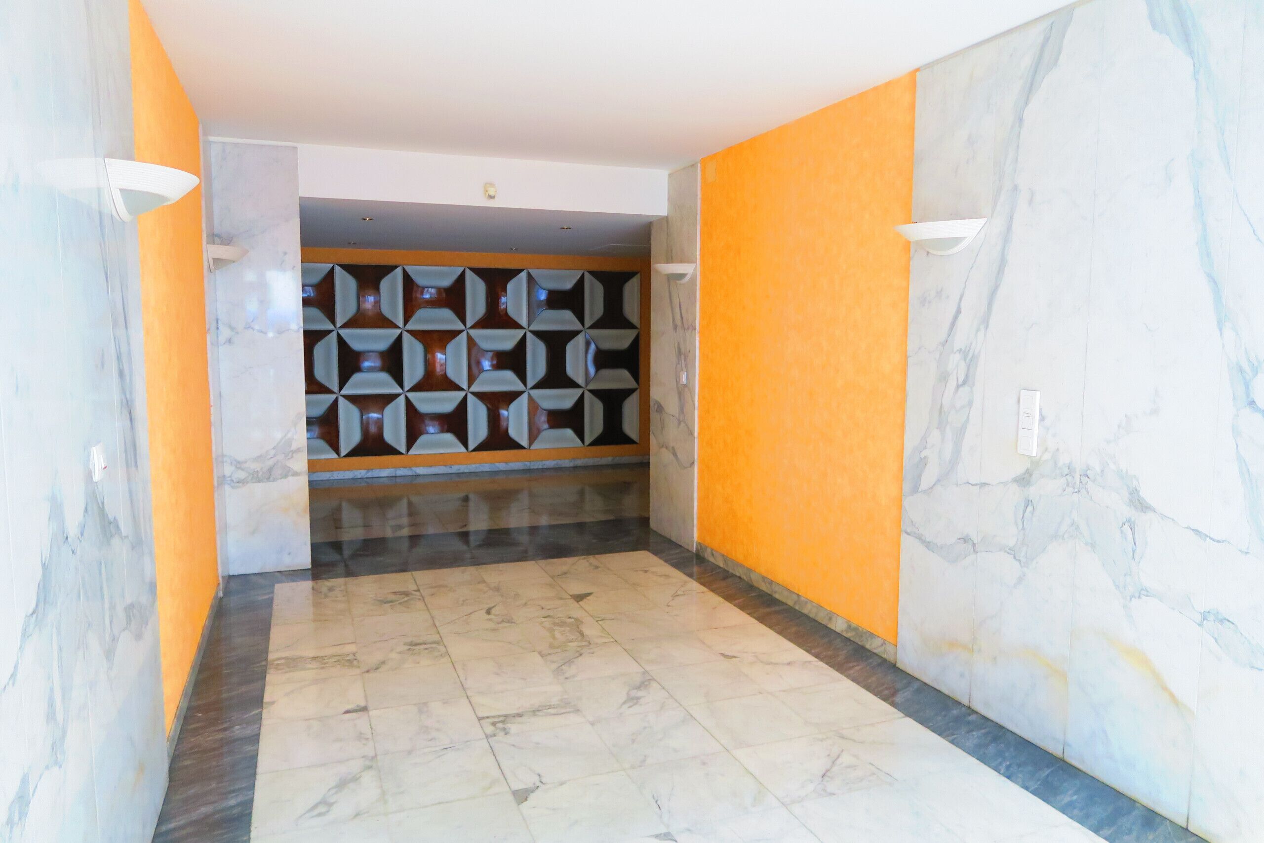 A hallway with marble walls, a geometric patterned wall, and a tiled floor.