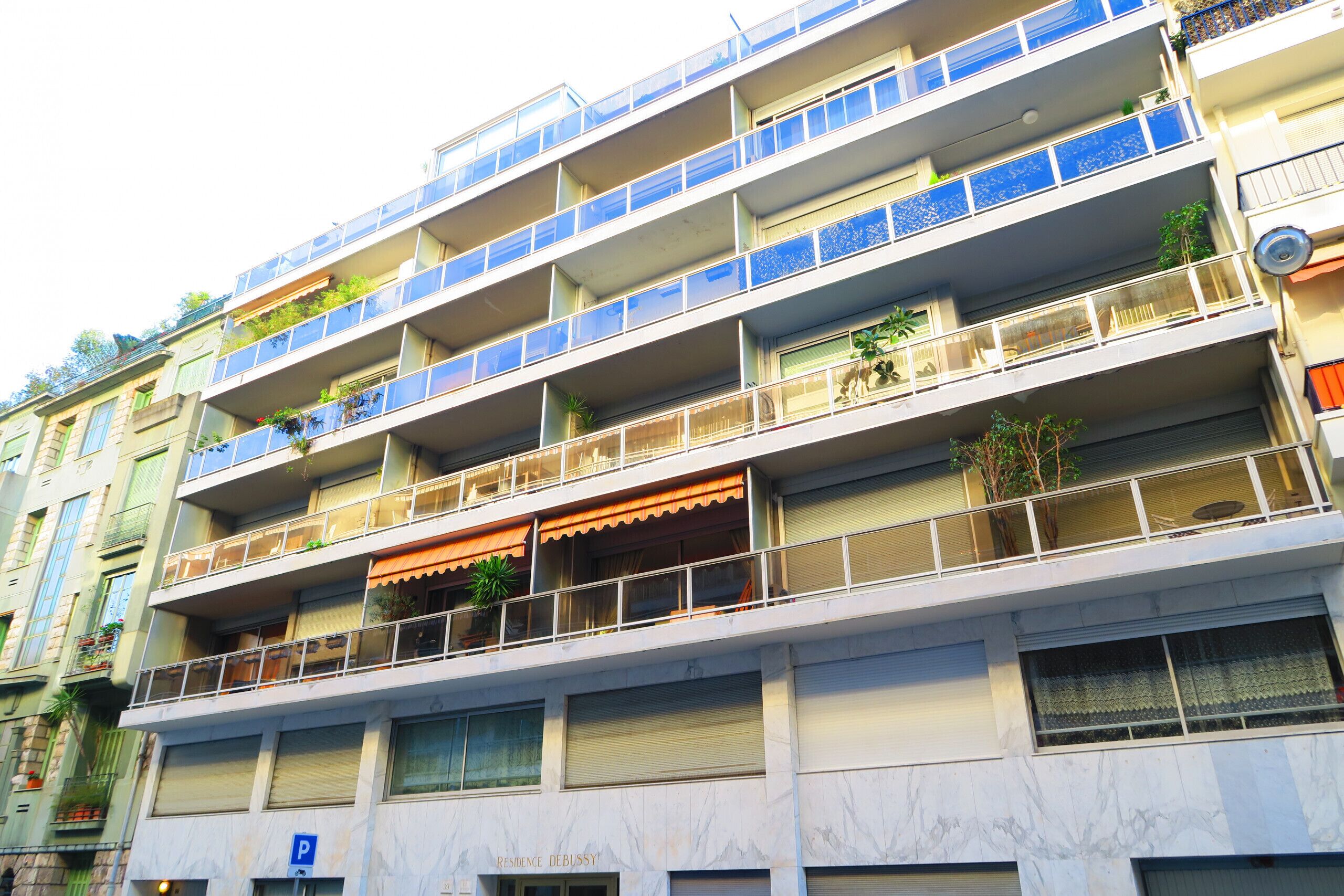 A multi-story residential building with balconies, some with plants.