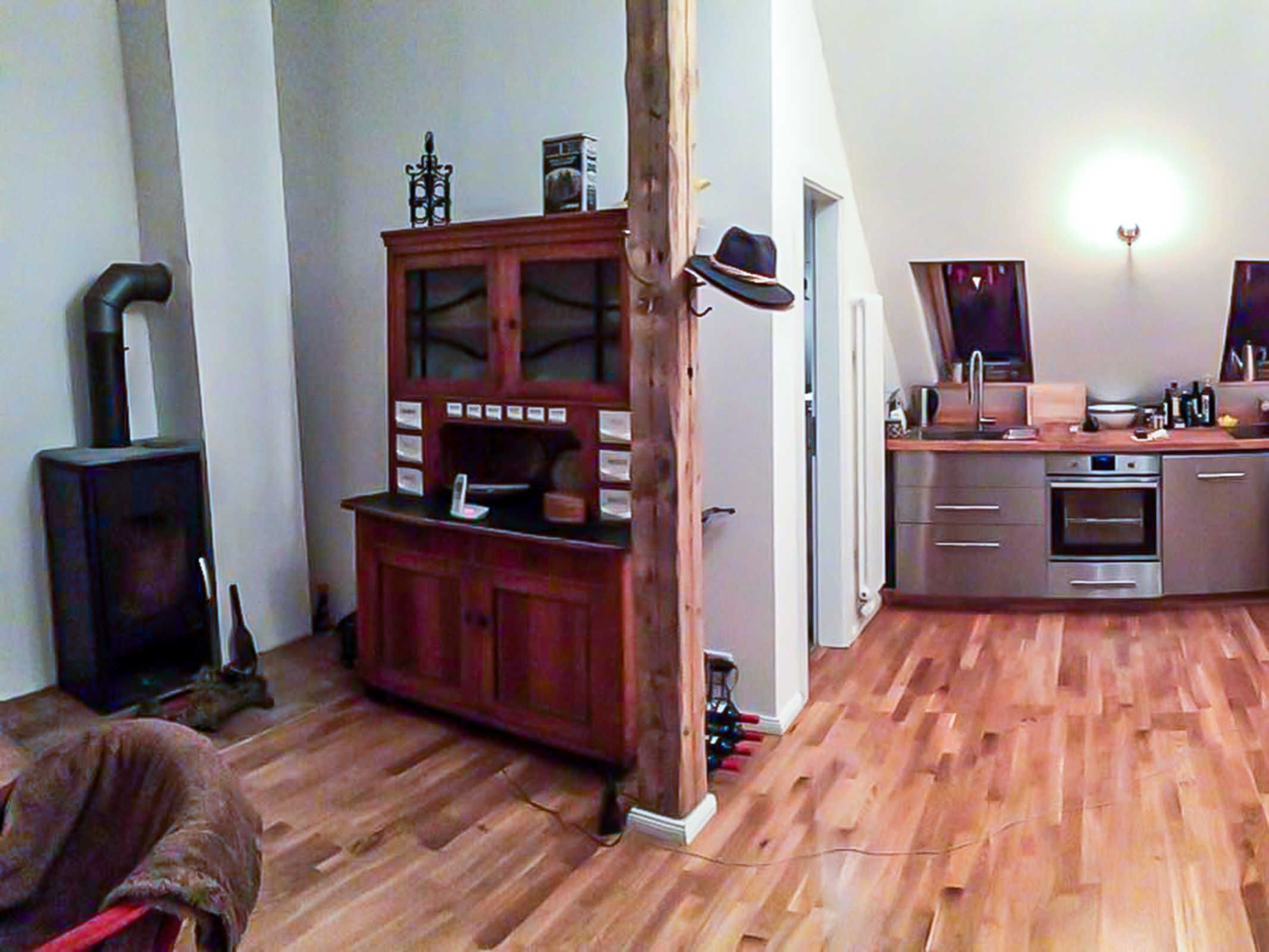 Une pièce dotée d’un plancher en bois, d’une armoire aux portes vitrées, d’une cheminée et d’un coin cuisine avec un évier et un four.