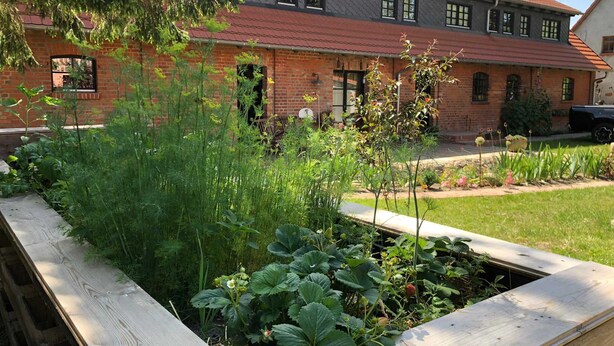 Ein Haus aus Ziegeln mit rotem Dach und einem Garten im Vordergrund.