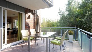 Ein Balkon mit Tisch, Stühlen, einer Topfpflanze und Blick auf Bäume.