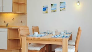 Ein Essbereich mit Holztisch und -stühlen, eine Küche mit weißen Schränken und drei kleine Bilder mit Strandmotiv an der Wand.