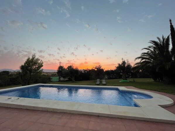 A swimming pool with a curved edge, surrounded by a paved area.