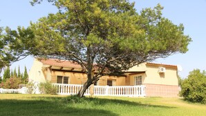 A two-story house with a white balcony, surrounded by a well-maintained lawn and trees.