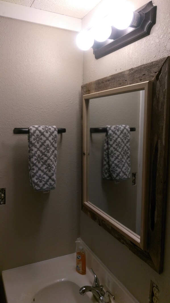 A bathroom with a white sink, a mirror with a wooden frame, and two patterned towels hanging on towel bars. - Charming Cabin 300 Yards from Free Boat Launch & Swimming Area (Broaddus)