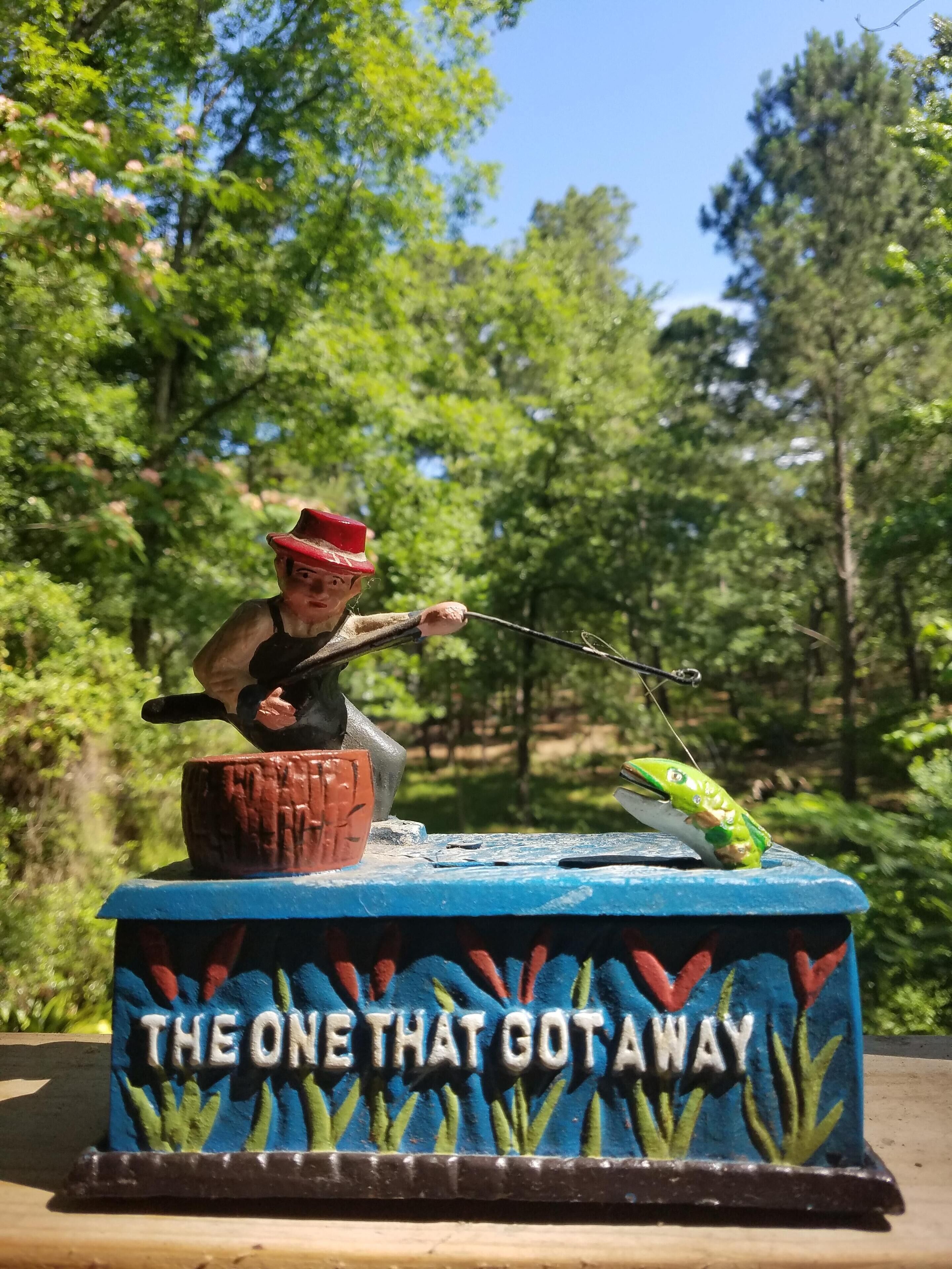 Eine Figur eines Mannes beim Angeln auf einem blau-roten Sockel, mit dem Text "THE ONE THAT GOT AWAY".