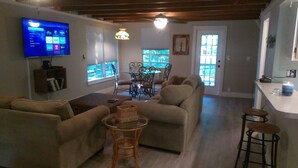 A living room with a television, a dining area with a table and chairs, and a kitchen counter with a water dispenser.
