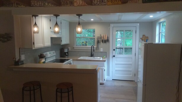 A kitchen with white cabinets, a central island with stools, pendant lighting, and a window with a view of greenery.