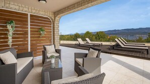 A covered outdoor seating area with wicker furniture and a glass table, overlooking a scenic view of mountains and a body of water. - Gorgeous home in Polje (Polje)