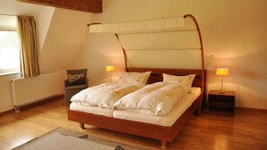 Ein Bett mit Baldachin, ausgestattet mit weißen Leinen, einem Holzkopfstück und zwei Nachttischlampen.