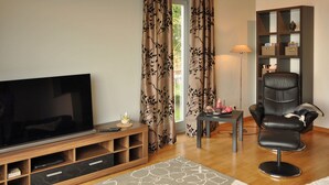 Ein Wohnzimmer mit Flachbildfernseher, Ledersessel, Bücherregal und einem Fenster mit Vorhängen.