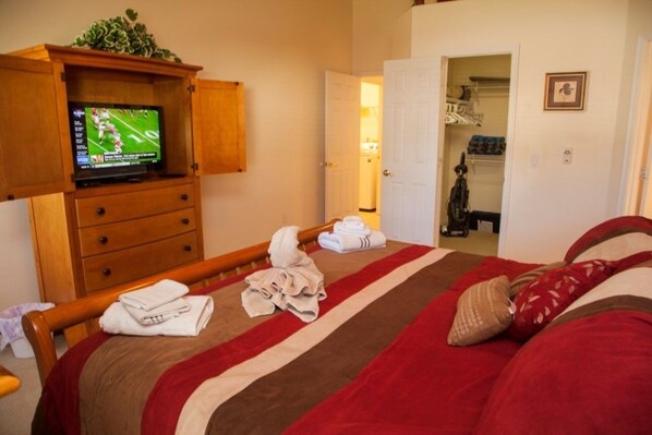 A hotel room with a bed, a television on a wooden cabinet, a closet, and a door leading to another room.