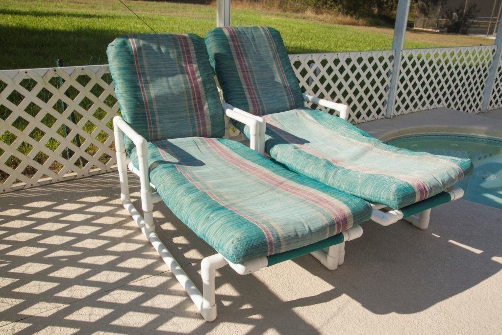 A sun lounger with striped cushions, a white lattice fence, and a pool in the background.