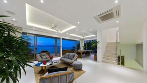 Un salon moderne avec un canapé, une table basse et un coin repas. Une grande fenêtre offre une vue sur la mer.