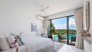 Une chambre avec un grand lit, un ventilateur de plafond, une vue sur la plage et un balcon avec une chaise.