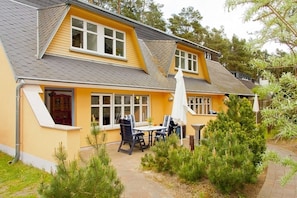 A yellow house with a sloped roof, a patio with a table and chairs, and a small garden area.
