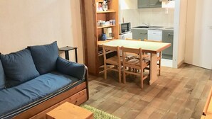 A compact living space with a sofa, a small table, a wooden dining table with chairs, a kitchen area with cabinets and appliances, and a door leading to another room. - Studio with mountain and lake view, Tignes (Tignes)