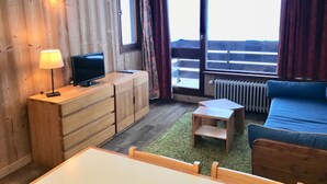 A room with wooden walls, a television on a wooden cabinet, a sofa, a small table, and a view of a balcony through large windows. - Studio with mountain and lake view, Tignes (Tignes)