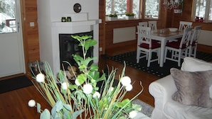 A cozy cabin interior with a fireplace, dining table, and white furniture.
