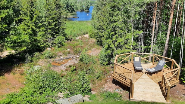 A wooden deck with two lounge chairs overlooking a forested area and a river.