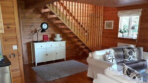 A cozy cabin interior with a wooden staircase, white furniture, and a clock on the wall.
