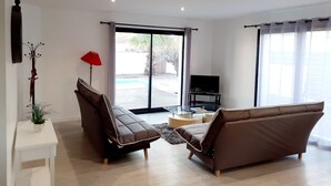Un salon moderne avec deux canapés, un téléviseur et une porte vitrée donnant sur un espace extérieur.