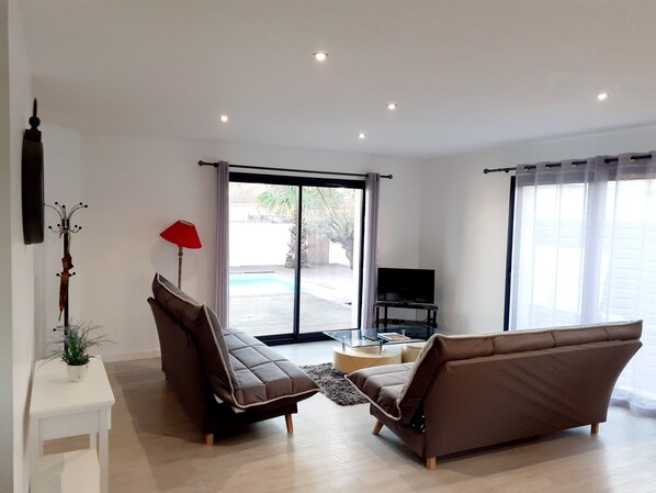 A modern living room with two sofas, a TV, and a glass door leading to an outdoor area.