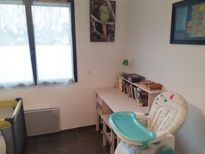 A child's room with a high chair, a bookshelf, and a window with curtains.