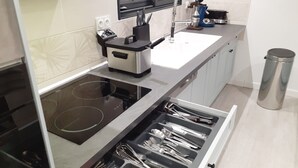 Une cuisine moderne équipée d’une plaque de cuisson à induction, d’un four encastré, d’une machine à café et d’une poubelle en acier inoxydable.