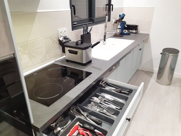 Uma cozinha moderna com fogão por indução, forno embutido, cafeteira e um cesto de lixo de aço inoxidável.