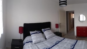 Une chambre à coucher avec un lit, des tables de chevet, une commode rouge et un tableau au mur.