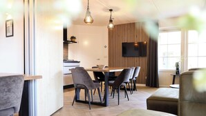 Ein modernes Wohnzimmer mit einem Holzesstisch, grauen Polsterstühlen, einem Ledersofa und einem flachbildfernseher an der Wand.