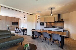 Una sala moderna con sofá, mesa de comedor y sillas, una cocina con armarios de madera y electrodomésticos, además de iluminación colgante.
