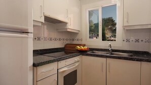 Une cuisine compacte avec des meubles blancs, un plan de travail en granit, un four encastré et une fenêtre donnant sur la verdure.