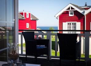 Un balcón con sillas de mimbre, una mesa y vista a casas rojas y el océano.