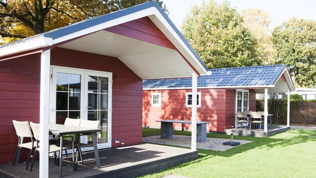 A red building with a covered patio area, a table with chairs, and a small garden. - Veluwe lounge for four people (Voorthuizen)