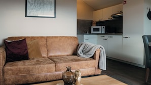 A living room with a brown sofa, a coffee table with decorative items, a kitchen area with white cabinets and a microwave. - Veluwe lounge for four people (Voorthuizen)