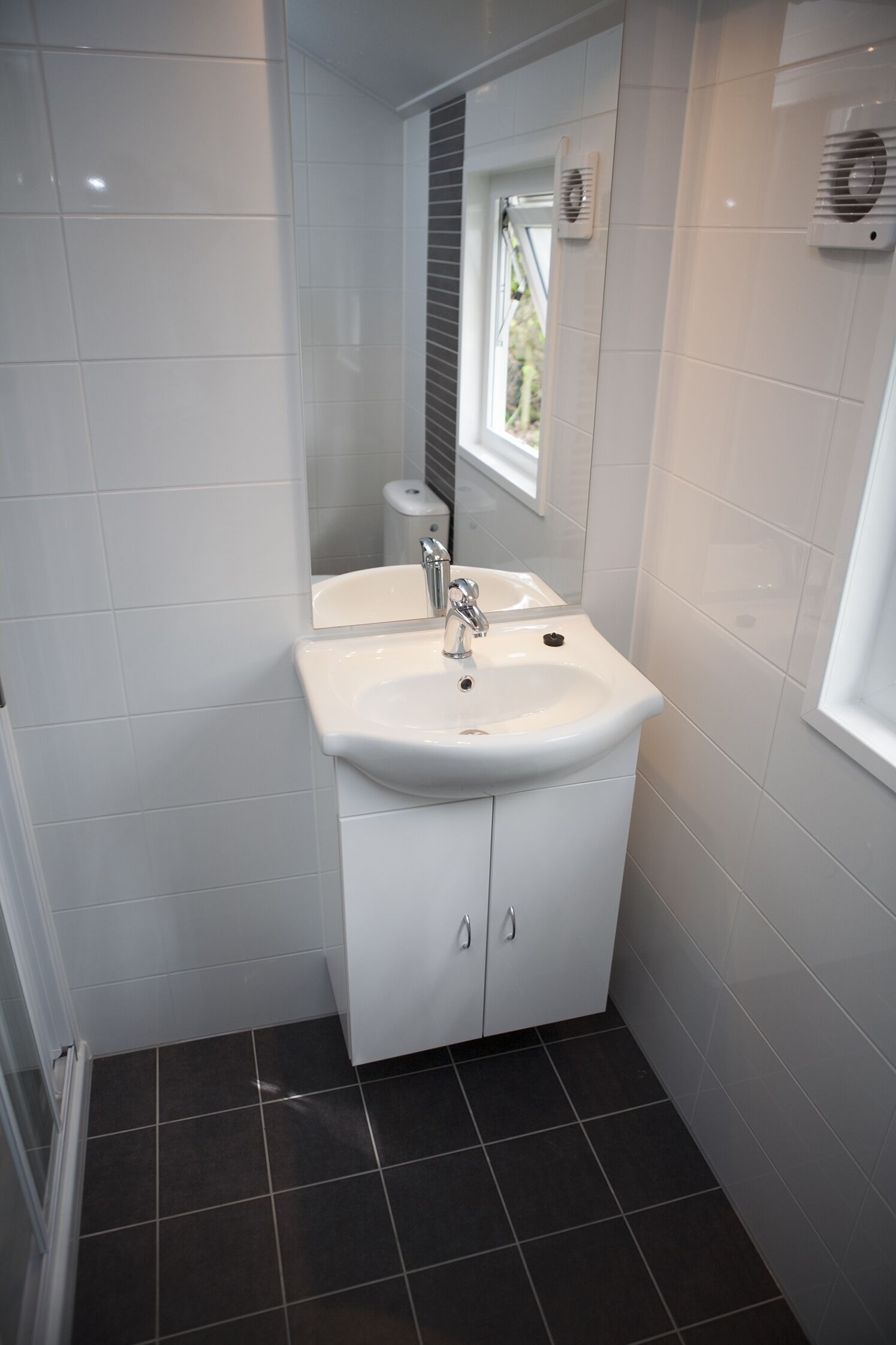 Ein Badezimmer mit einem weißen Waschbecken, einem Spiegel und einem Fenster.
