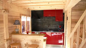 A wooden cabin interior with a kitchen area featuring red cabinets, a wooden bar with stools, and a decorative heart-shaped lamp. - Typical Savoyard chalet, independent, warm and cozy (Thônes)
