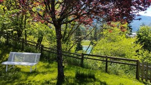 A bench in a lush green area with a wooden fence and a mountain in the background. - Typical Savoyard chalet, independent, warm and cozy (Thônes)