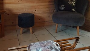A wooden cabin interior with a wooden bench, a small ottoman, a chair with a decorative pillow, and a window overlooking a forested area. - Typical Savoyard chalet, independent, warm and cozy (Thônes)