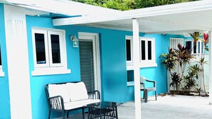 A house with a blue exterior, white windows, and a covered patio area with a table and chairs. - Queen apartment with generator, washing machine & patio furniture for relaxation (Nassau)