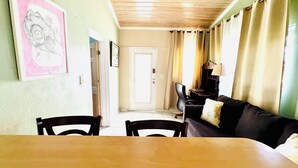 A dining area with a table and chairs, a sofa with a cushion, a lamp, and a door leading to another room. - Queen apartment with generator, washing machine & patio furniture for relaxation (Nassau)