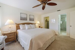 A bedroom with a large bed, two bedside tables with lamps, a ceiling fan, and a door leading to a bathroom.