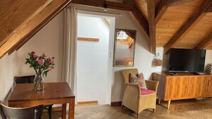 Una habitación cálida en el ático con una mesa de madera, una silla de mimbre, un televisor y un espejo en la pared.