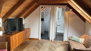 Una habitación cálida en el ático, con techo de madera, un televisor sobre un mueble de madera, un sofá y suelo con patrón de espiga.