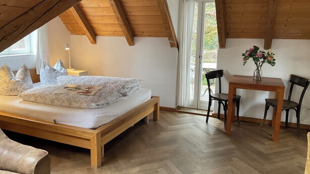 Un dormitorio con cama de madera, una mesita de noche, un escritorio con sillas y vistas a través de una ventana.