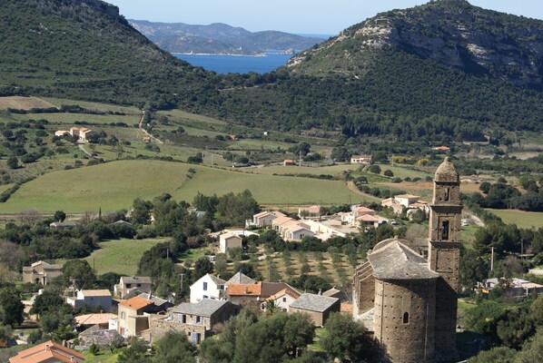 A rural village with a prominent church tower, surrounded by green fields and a body of water in the distance.