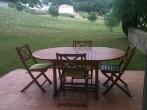 A round wooden table with four chairs, set on a brick patio with a grassy lawn and trees in the background. - comfortable rental type f2 in the heart of the vineyard with swimming pool (Patrimonio)
